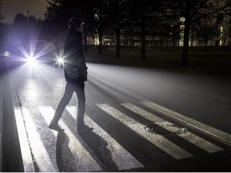 Fußgänger im Scheinwerferlicht bei Nacht Ein Fußgänger geht nachts über einen Fußgängerüberweg im Scheinwerferlicht eines Autos.